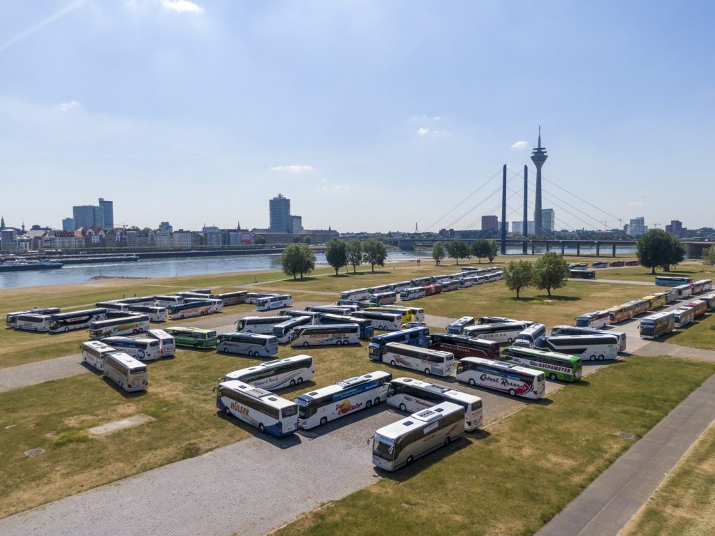 Drohnenaufnahme mehrerer Busse mit dem Rhein und Düsseldorf im Hintergrund